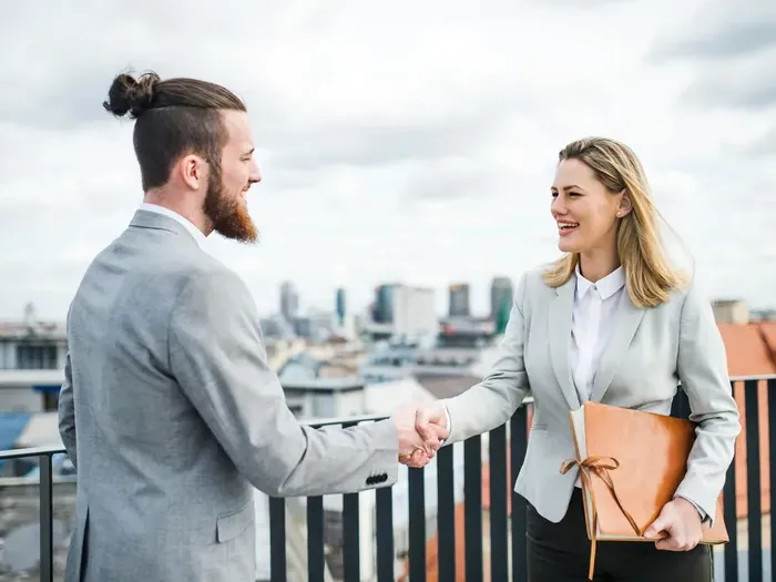 Two professionals shaking hands on a rooftop terrace after a meeting with city skyline visible